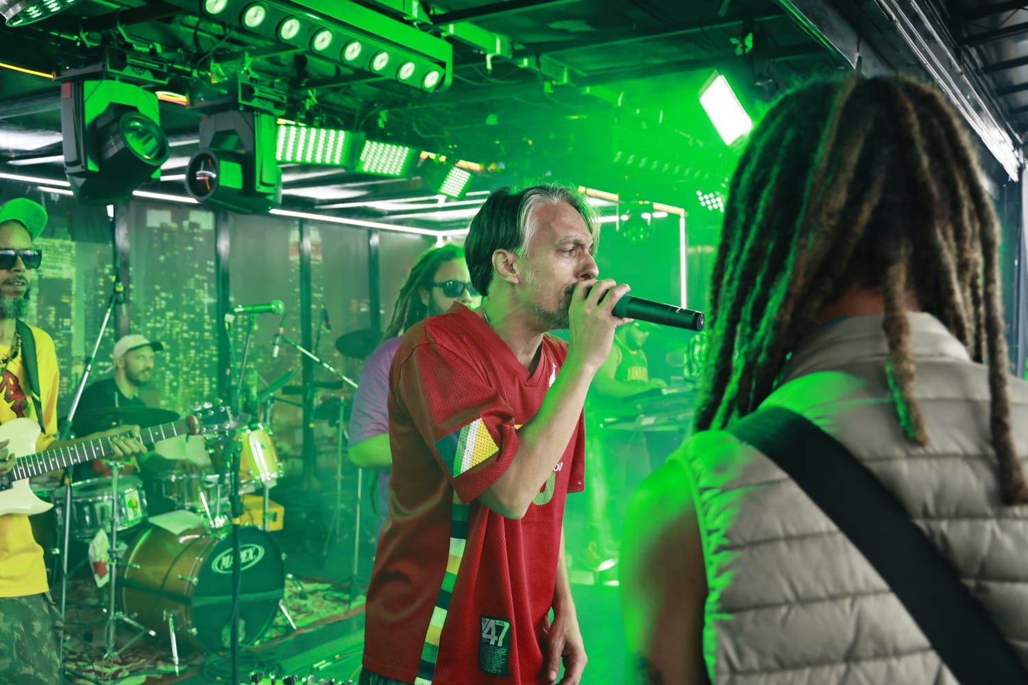 Brasil Riddim se apresentando ao vivo sob luzes verdes em uma casa de shows em Brasília